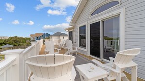 A deck with white Adirondack chairs and a table, overlooking a residential area with houses. - 1522 - Sand Dollar - Oceanside Corolla Home w/ Pool & Volleyball (Corolla)