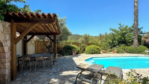 Eine Terrasse mit Pool, Steinboden, einer Pergola und Sitzgelegenheiten im Freien.