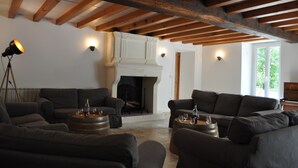 Un salon chaleureux avec des canapés sombres, une cheminée et des poutres en bois au plafond.