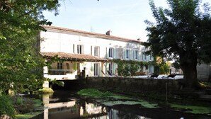 Un bâtiment situé au bord de la rivière, avec un pont, et entouré de verdure.