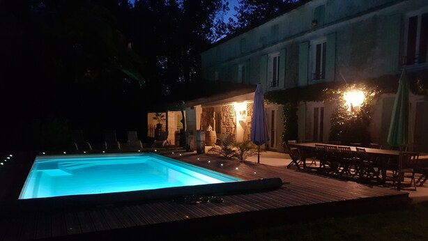 Une piscine dotée d’une terrasse en bois, entourée de mobilier d’extérieur et bordée d’un bâtiment en pierre.