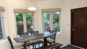 A dining area with a wooden table, six chairs, and a bench. There are two windows with blinds, a door, and a ceiling light.