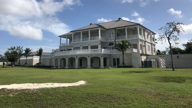 A large, multi-story building with a covered balcony area and a lawn in the foreground.