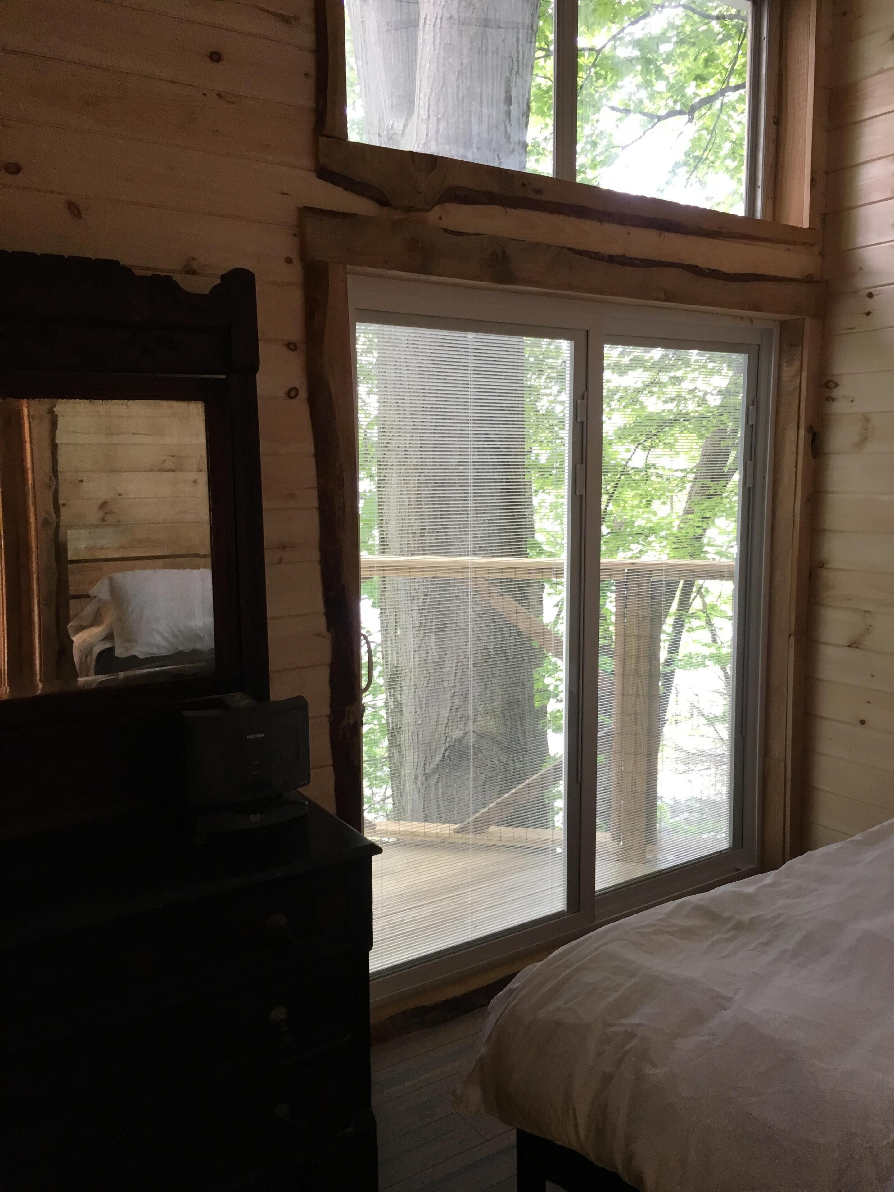 Un dormitorio con cama, cómoda y una ventana grande con vistas a árboles.