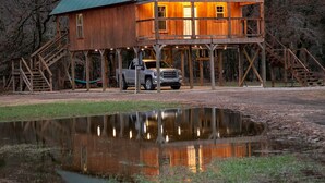 A wooden cabin with a green roof, situated by a reflective pond, surrounded by trees. - Majestic Moose Lodge- Oark Cabin Rentals (Oark)