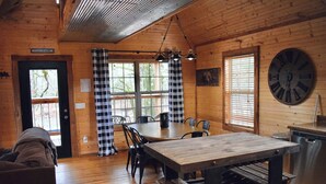 A cozy cabin interior with a wooden dining table, chairs, a bench, a large wall clock, and a kitchen area with a sink and stove. - Majestic Moose Lodge- Oark Cabin Rentals (Oark)