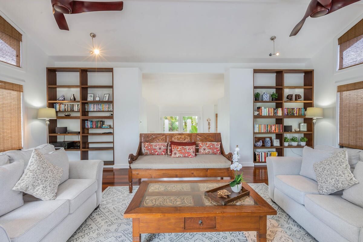 Un salon spacieux comprenant un ensemble de canapés, deux tables d’appoint et une table basse. On y trouve également deux grandes étagères remplies de livres et d’objets décoratifs.