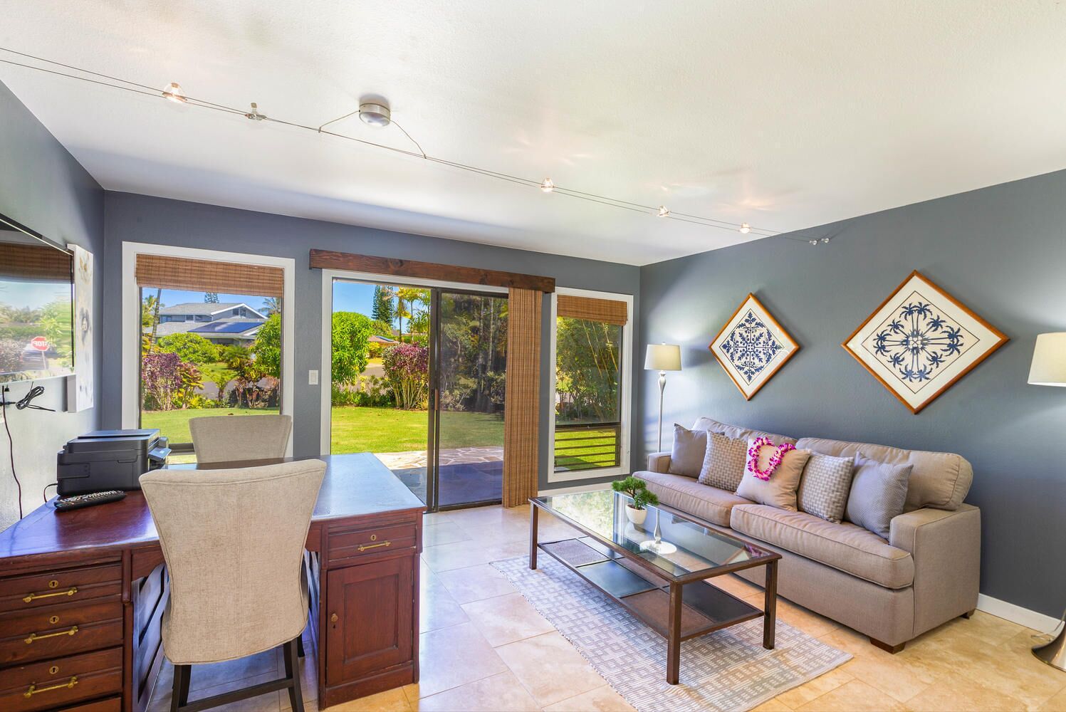 A modern living room with a sofa, coffee table, and a desk with a chair. There are large sliding glass doors leading to a garden.