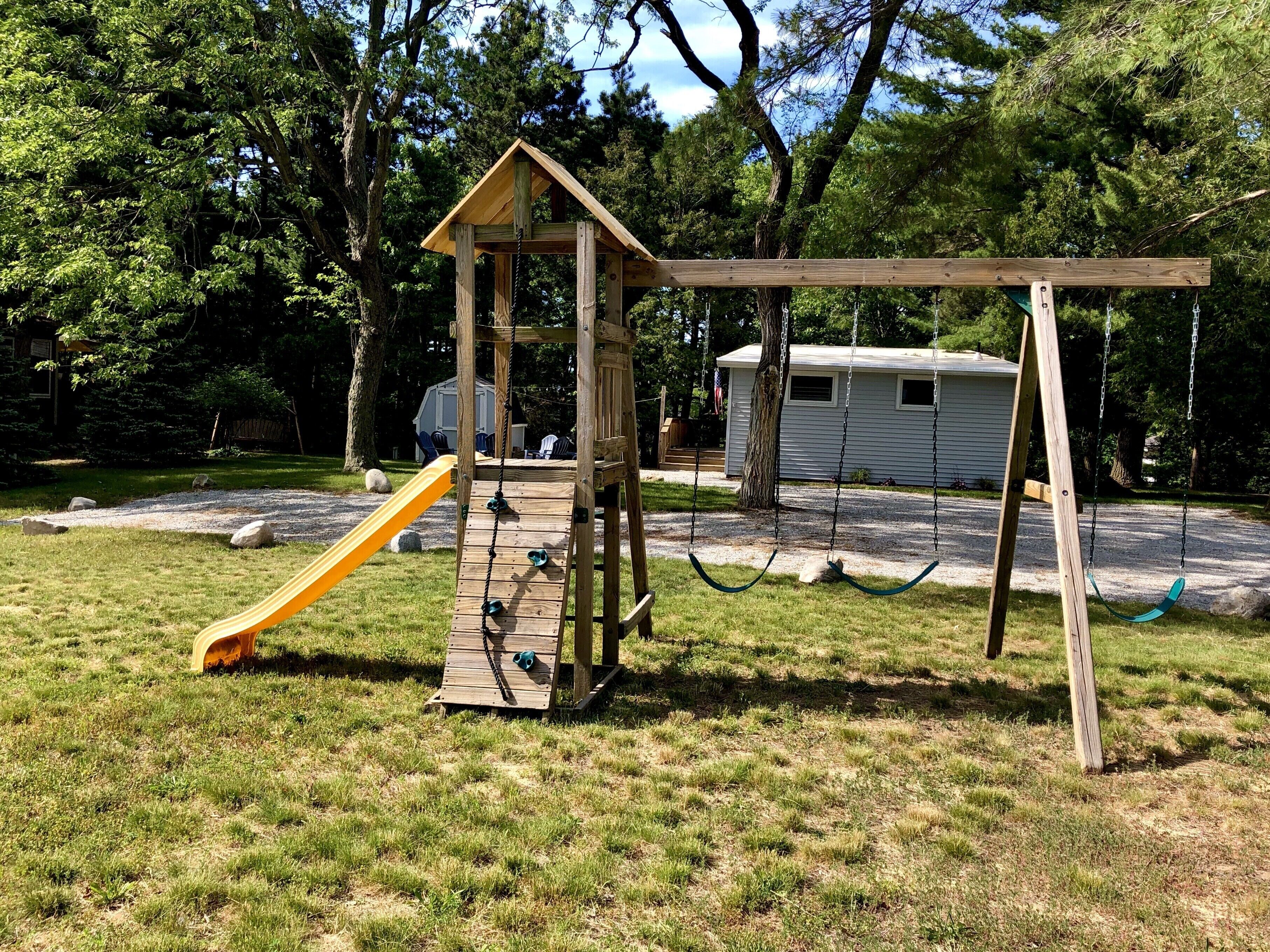 A wooden play structure with a slide and swings in a grassy park area.