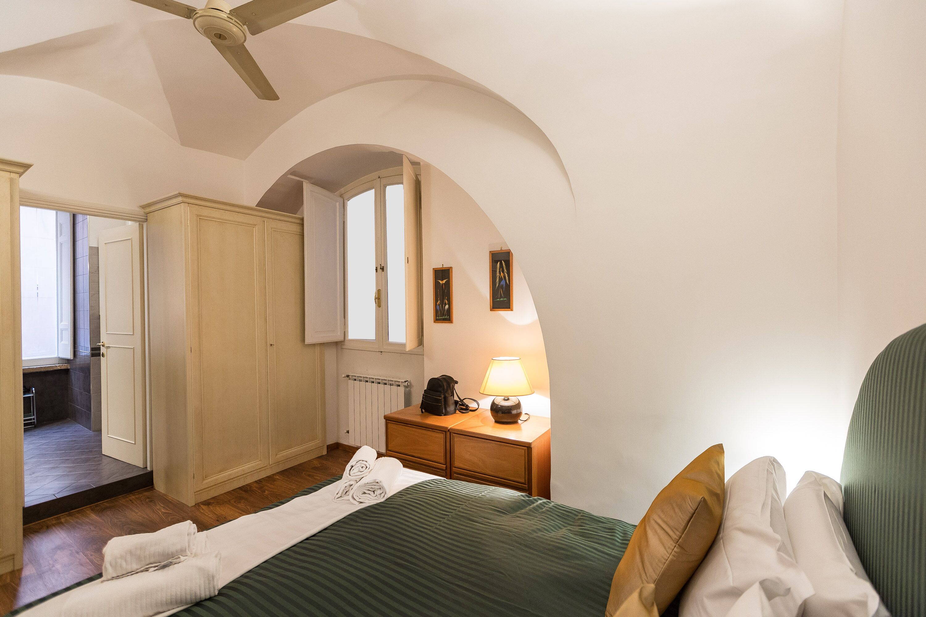 Un dormitorio con cama, mesita de noche, lámpara, armario y techo abovedado.