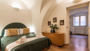 A bedroom with a curved ceiling, a bed with green bedding, a wooden dresser, and a potted plant. - Lovely New home, via Nazionale . (Roma)