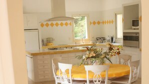 A bright kitchen with white cabinets, a yellow countertop, and a dining area with white chairs and a yellow tablecloth. - 360 m2 house (Meynes)