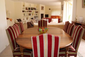 A dining room with a wooden table surrounded by striped chairs, a bookshelf, and a television in the background. - 360 m2 house (Meynes)