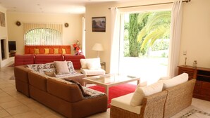 A living room with a brown sofa, a wicker sofa, a glass coffee table, and a red rug. - 360 m2 house (Meynes)