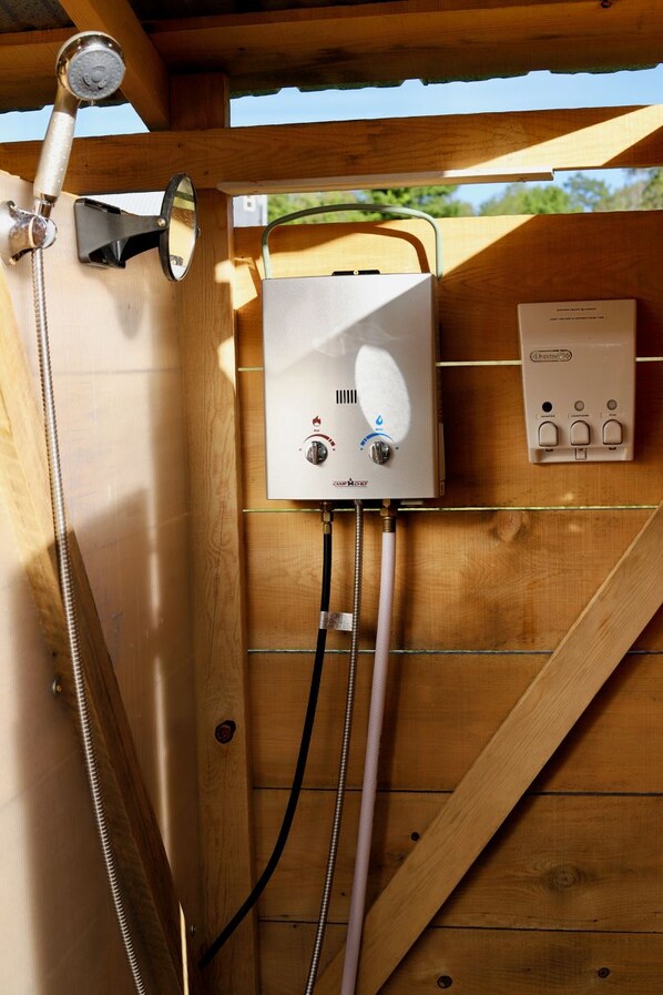 Una estructura de madera con calentador de agua, cabezal de ducha y panel de control.