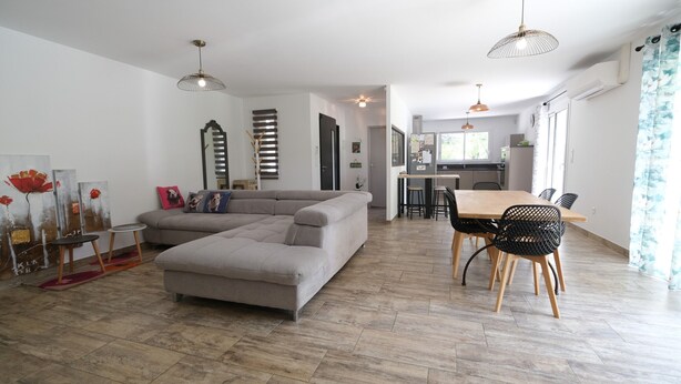 A modern living room with a sectional sofa, dining table with chairs, and pendant lighting.