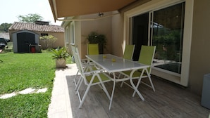 A patio with a table and chairs, a sliding glass door, and a small shed in the background.