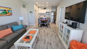 A modern living room with a sofa, coffee table, and TV. A dining area with a table and chairs is visible in the background. - RECENTLY REMODELED "The Surf Shack" 1st Floor, Overlooks Pond, Close to Beach (Corpus Christi)