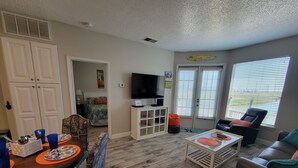 A living room with a dining area, a TV, and a window with blinds. - RECENTLY REMODELED "The Surf Shack" 1st Floor, Overlooks Pond, Close to Beach (Corpus Christi)