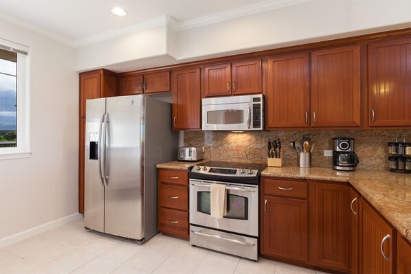 A modern kitchen with stainless steel appliances, wooden cabinets, and a granite countertop.