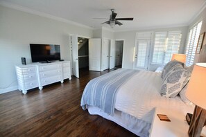 Une chambre avec un grand lit, une télévision, une commode et un ventilateur de plafond.