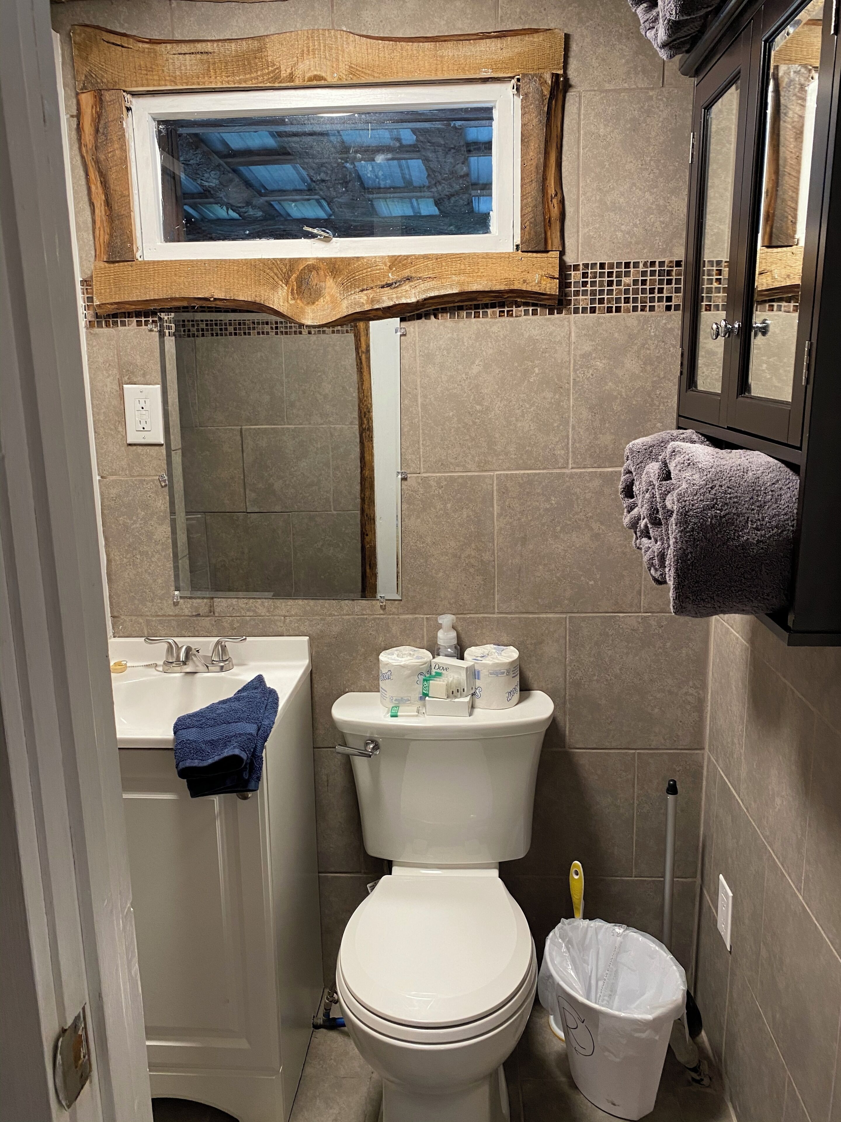 Une salle de bain avec des toilettes, un lavabo et une fenêtre située au-dessus du miroir.