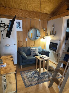 A cozy cabin interior with a blue sofa, a small wooden table, a mirror, and a ladder.