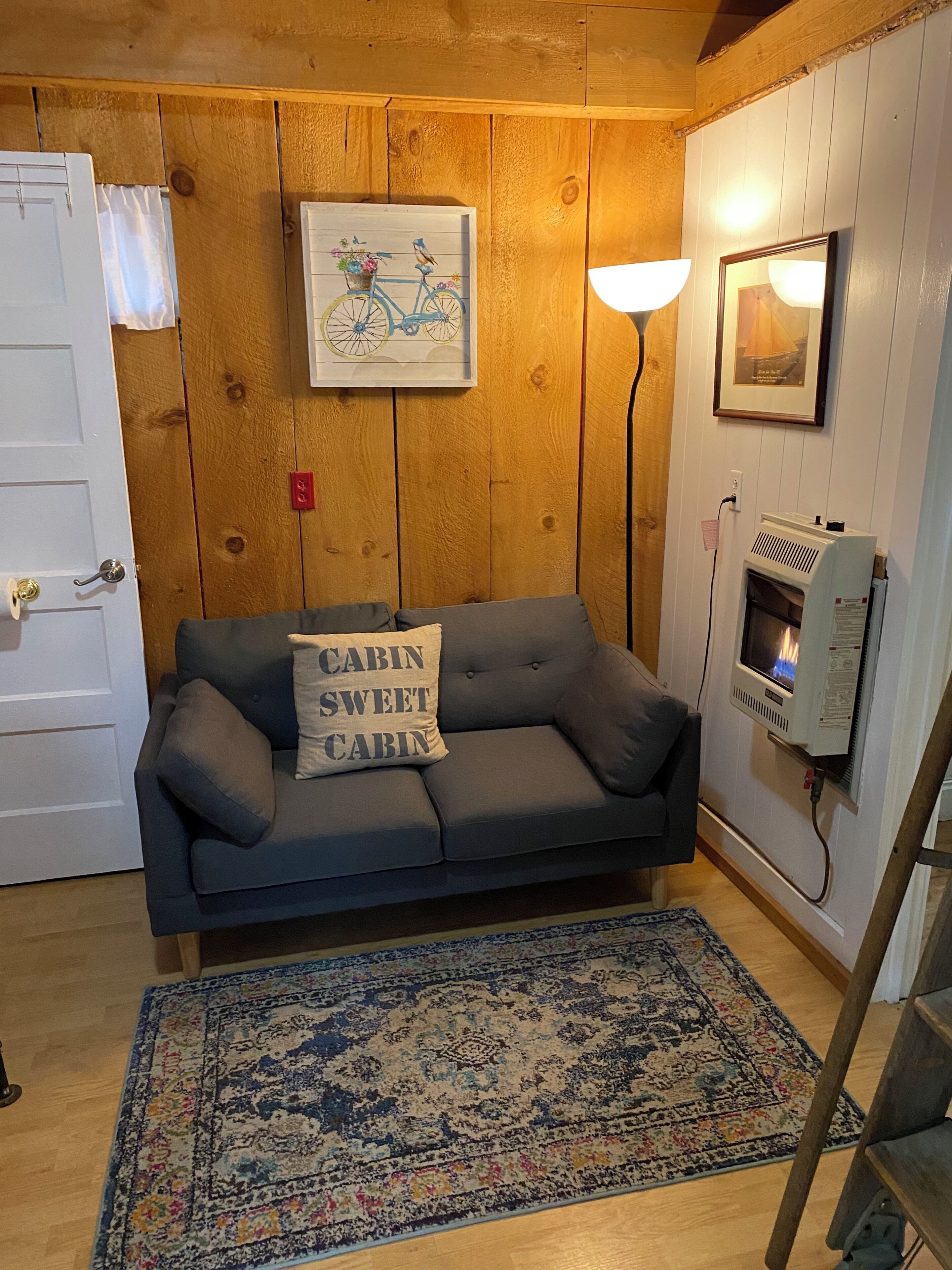 L’intérieur d’un chalet chaleureux, avec un canapé gris, un tapis à motifs, des murs en bois, une cheminée et un tableau encadré accroché au mur.