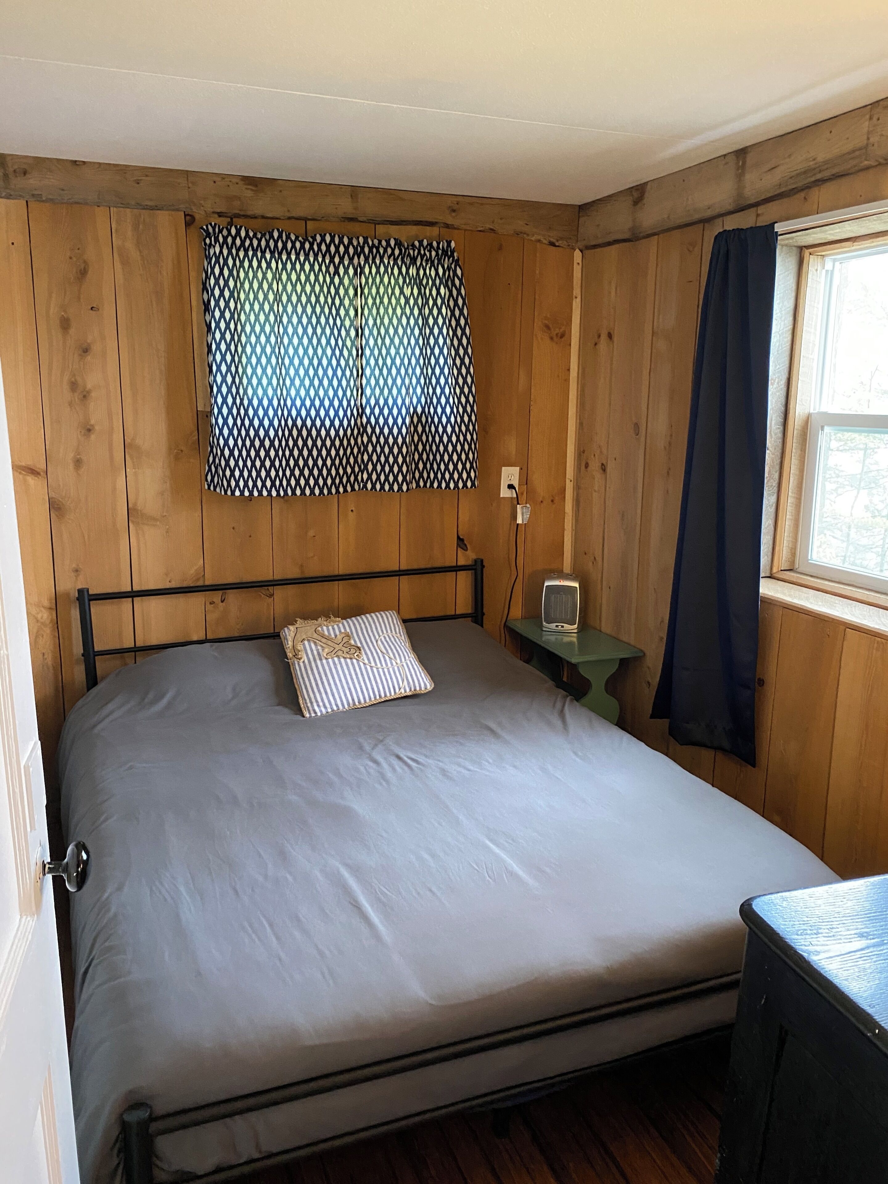 A room with a bed, a small table, a window with curtains, and wooden walls.