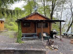 Une cabane rustique avec une façade en bois, un petit porche doté de bancs et un espace barbecue.