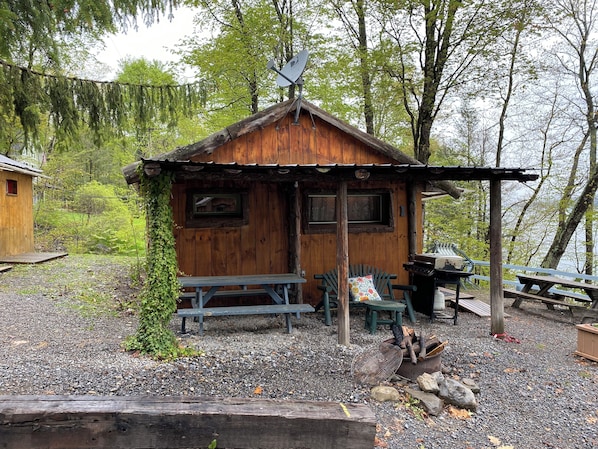 A rustic cabin with a wooden exterior, a small porch with benches, and a grill area.