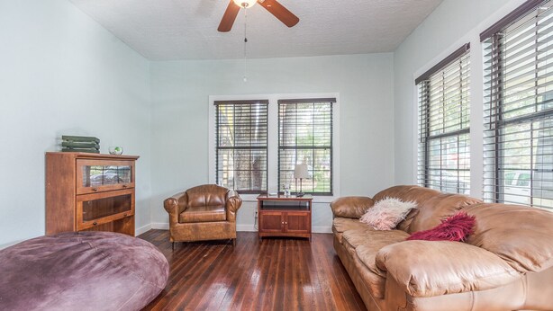 A living room with a wooden floor, a brown leather sofa, a purple ottoman, a wooden cabinet, and a ceiling fan. - Pet friendly 1bd/1b unit with living space and full kitchen (Gainesville)