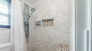 A bathroom with white marble tiles, a shower with a glass door, and a small decorative shelf. - Pet friendly 1bd/1b unit with living space and full kitchen (Gainesville)