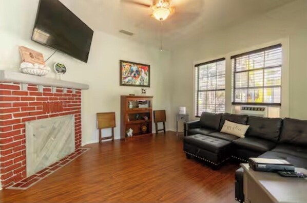 A living room with a fireplace, a black leather sofa, a television, and a large window.
