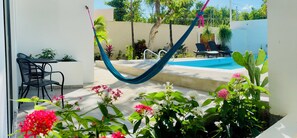 Un espace aménagé au bord de la piscine, avec un hamac, des chaises longues et des plantes en pot.