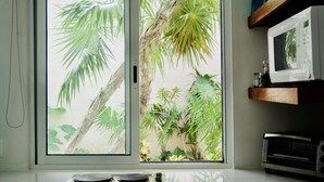 A kitchen with a sliding glass door leading to a tropical garden view, a microwave, and a toaster oven. - AQUA GUESTHOUSE 3~ STEPS FROM THE BEACH ~ POOL ~ A+ INTERNET (Puerto Morelos,)