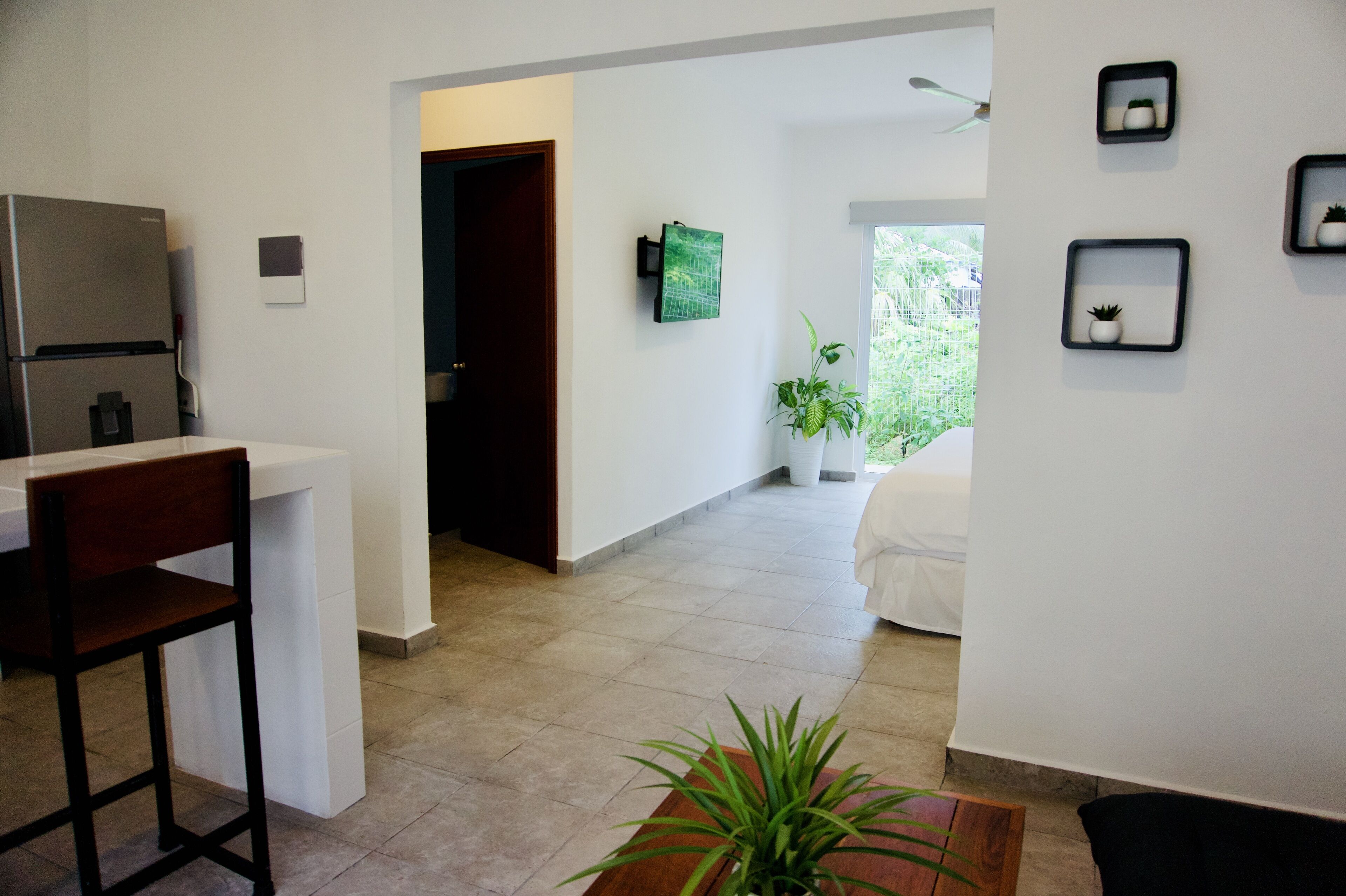 A modern kitchen with a refrigerator, a dining area with a chair, and a hallway leading to a bedroom.