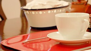 A white cup on a red saucer and a white bowl with a handle on a table. - Zilbetinea (Baztan)