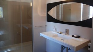 A modern bathroom with a glass shower enclosure, a white sink with a black countertop, and a large mirror with a black frame. - Zilbetinea (Baztan)
