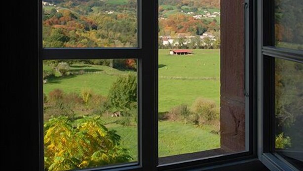 A window with a view of a hilly landscape, including green fields and distant buildings. - Zilbetinea (Baztan)