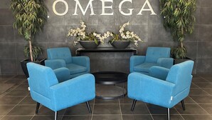 A reception area with a modern design, featuring two blue chairs, a black table, and a wall-mounted sign that reads "OMEGA".