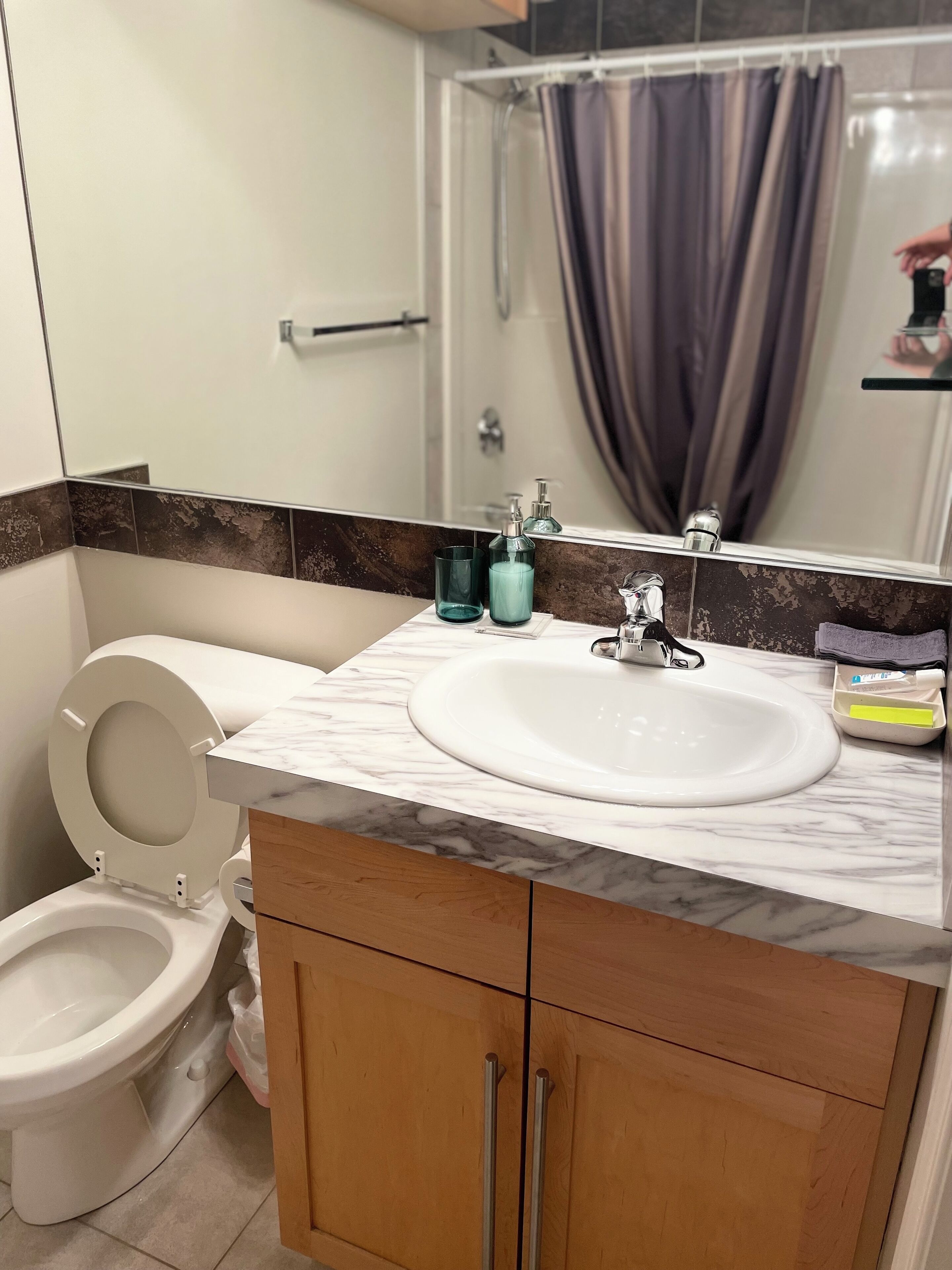 A bathroom with a white toilet, a sink with a marble countertop, and a wooden cabinet.