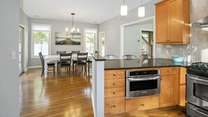 A modern kitchen with wooden cabinets, stainless steel appliances, and a dining area with a table and chairs. - Alex`s Pool House Private Pool & Hot Tub Centrally Located in the Saugatuck Douglas Area (Douglas)