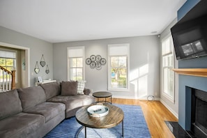 A living room with a gray sectional sofa, a round coffee table, a fireplace, and a TV mounted on the wall.