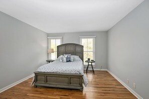 A bedroom with a bed, two windows, a nightstand, and a small table. - Alex`s Pool House Private Pool & Hot Tub Centrally Located in the Saugatuck Douglas Area (Douglas)