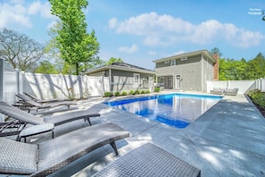 A residential backyard with a swimming pool, lounge chairs, and a covered patio area.