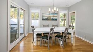 A dining room with a white table, six chairs, and a painting above the table. - Alex`s Pool House Private Pool & Hot Tub Centrally Located in the Saugatuck Douglas Area (Douglas)