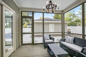 A covered porch with wicker furniture, a chandelier, and large windows.
