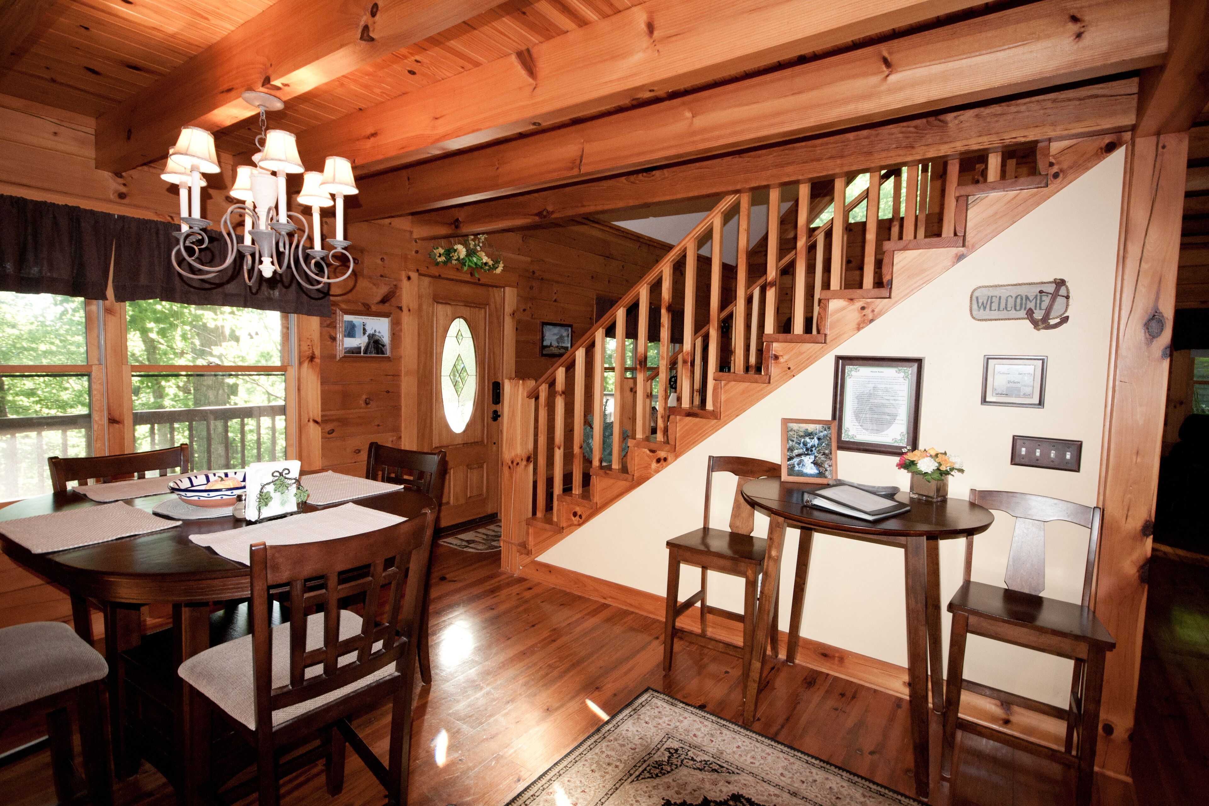 Un intérieur en bois comprenant une table à manger, des chaises, un lustre, un escalier et une pancarte de bienvenue.