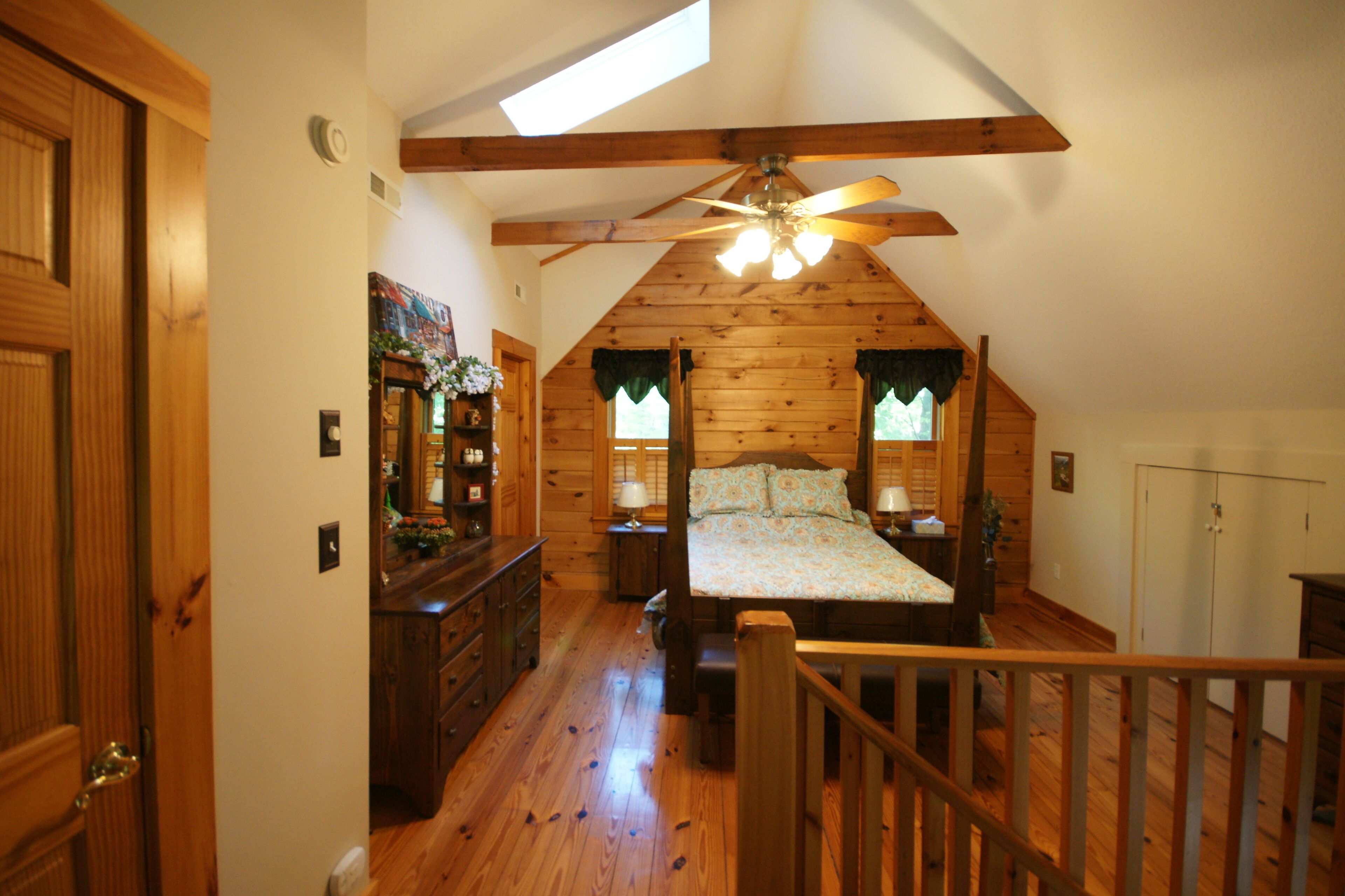 A bedroom with a sloped ceiling, wooden walls, a bed with a floral bedspread, two nightstands, and a ceiling fan.